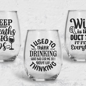 May include: Three clear glass wine glasses with black vinyl lettering. The first glass says "Deep Breaths Big Sips" with a small wine glass icon. The second glass says "I used to think drinking was bad for me so I gave up thinking". The third glass says "Wine is like a duct tape it fixes everything".
