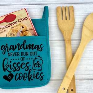 May include: Teal blue oven mitt with a pocket, featuring the text "grandmas never run out of kisses or cookies" in black. A bag of chocolate chip cookie mix is in the pocket.