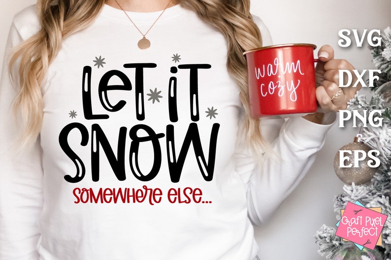 May include: White long-sleeved shirt with black text that reads "Let it snow somewhere else..." A red mug with white text that reads "warm cozy" is being held by a person wearing the shirt.