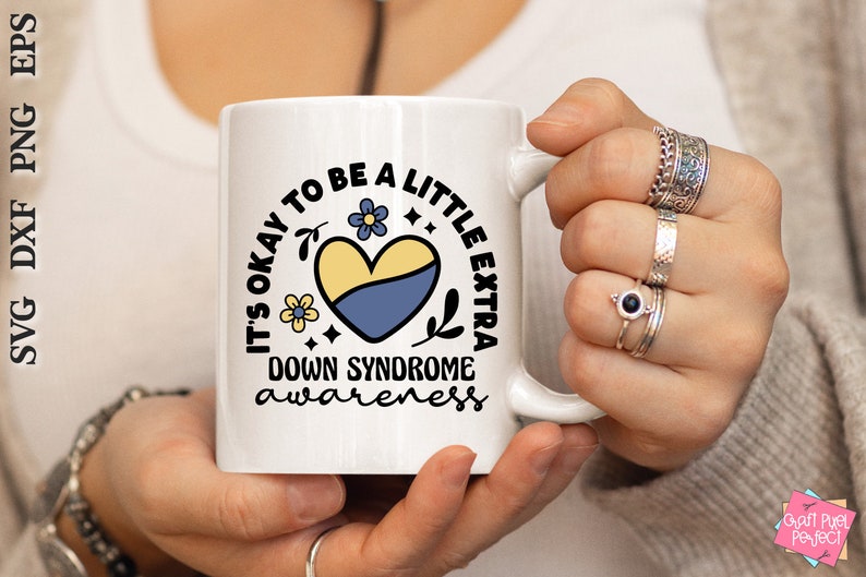 May include: White ceramic mug with a blue and yellow heart and the text "It's okay to be a little extra Down Syndrome awareness".