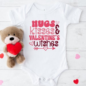 May include: White baby onesie with the text "hugs kisses & valentine's wishes" in pink and red lettering with a pink arrow and hearts.