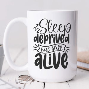 Puede incluir: Taza de cer&aacute;mica blanca con un dise&ntilde;o negro que dice "Sleep deprived but still alive".