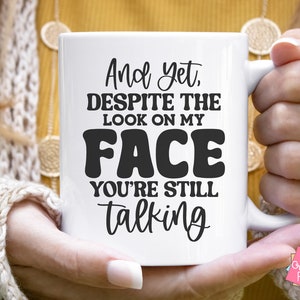 Puede incluir: Taza de cer&aacute;mica blanca con texto negro que dice "And yet, despite the look on my face you're still talking".