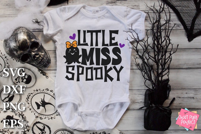 K&ouml;nnte beinhalten: Wei&szlig;er Baby-Strampler mit einem schwarzen Geistermotiv und dem Text "Little Miss Spooky" in Schwarz mit violetten Akzenten.