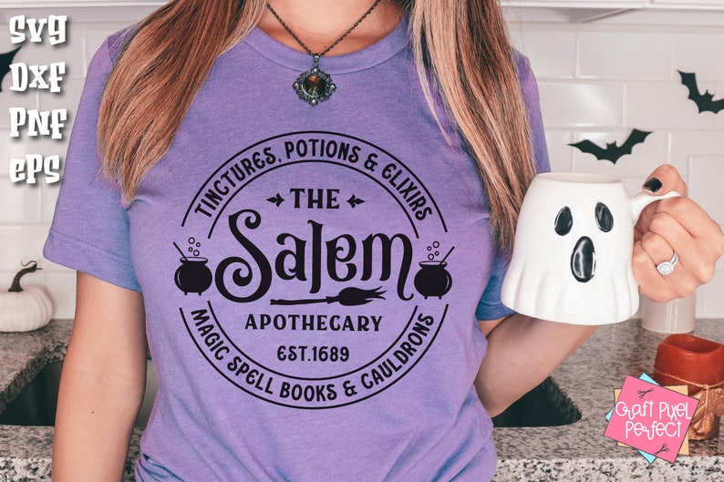 Pu&ograve; includere: Maglietta viola con un design circolare nero che dice "The Salem Apothecary Est. 1689" con immagini di calderoni e una scopa.