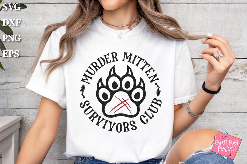 Pu&ograve; includere: Maglietta bianca con un design grafico nero e rosso. La grafica presenta un'impronta di zampa con il testo "Murder Mitten Survivors Club".