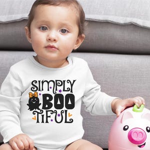 Pu&ograve; includere: Una maglietta bianca a maniche lunghe con il testo "Simply Boo-tiful" in nero con una grafica di un fantasma viola e arancione.