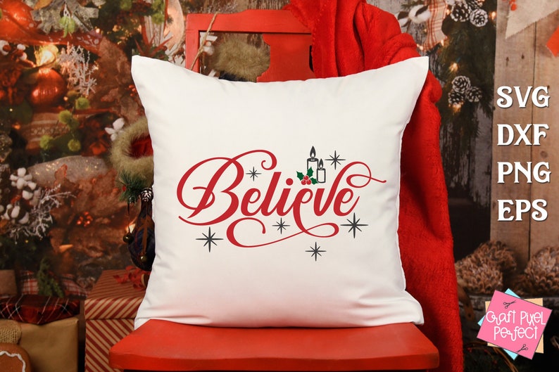 May include: White pillow with the word "Believe" in red cursive lettering, with a small image of candles and holly berries above the word. The pillow is on a red chair in front of a Christmas tree.