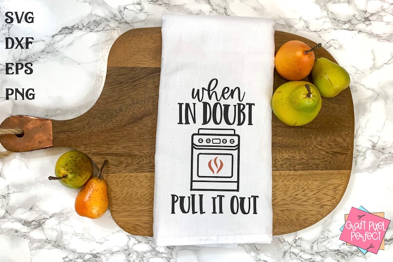 May include: White kitchen towel with black text that reads "When in doubt, pull it out."  A black and white illustration of a stove with a red flame is above the text. The towel is on a wooden chopping board with pears.