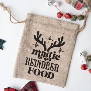 May include: A brown burlap gift bag with the text "magic reindeer food" in black lettering. The bag has a drawstring closure and is decorated with a black silhouette of reindeer antlers.