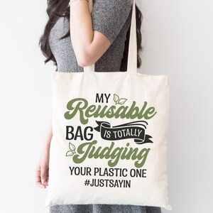 Pu&ograve; includere: Una borsa di tela bianca con un design verde e nero che dice "My Reusable Bag is Totally Judging Your Plastic One #JustSayin".
