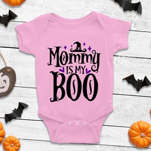 May include: Pink baby onesie with a black and purple graphic that says "Mommy is my Boo" with a witch's hat on top of the "O".