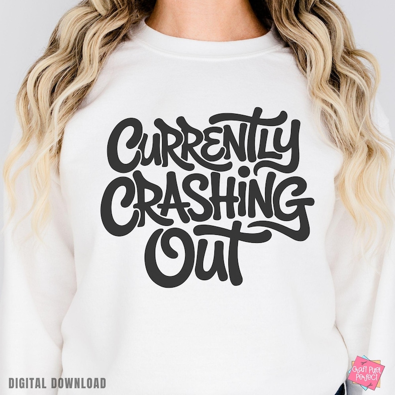 May include: White sweatshirt with the phrase "Currently Crashing Out" in large, black, stylized lettering. The words are in a bold, rounded font. The phrase "Digital Download" is at the bottom left.