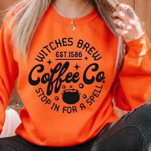 以下が含まれることがあります： 「Witches Brew Coffee Co.」というコーヒーショップの黒とオレンジのグラフィックデザインで、「Est. 1586」と「Stop in for a spell」のテキストが書かれています。