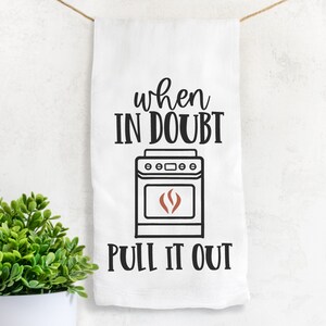 May include: White kitchen towel with black text that reads "When in doubt, pull it out."  A black and white illustration of a stove with a red flame is above the text.