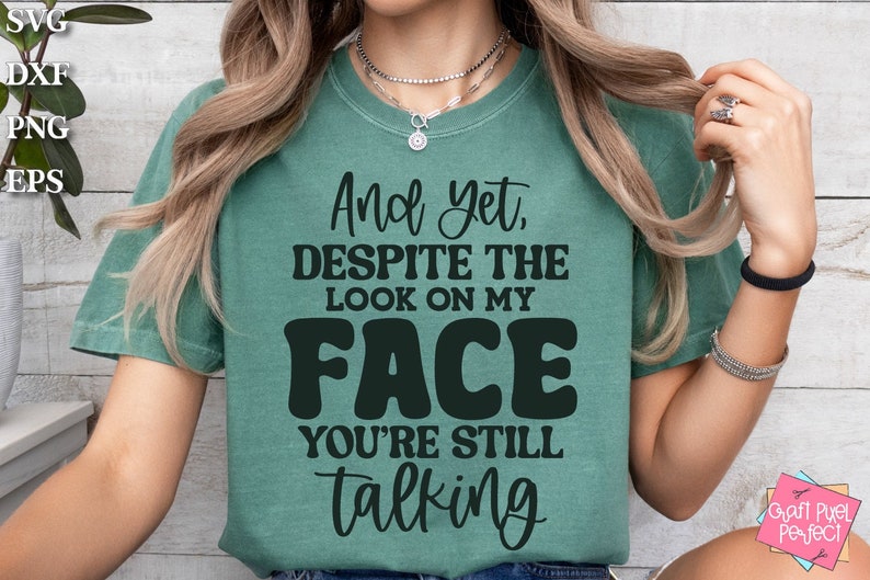 May include: A teal green t-shirt with the text "And yet, DESPITE THE LOOK ON MY FACE YOU'RE STILL talking" in black.