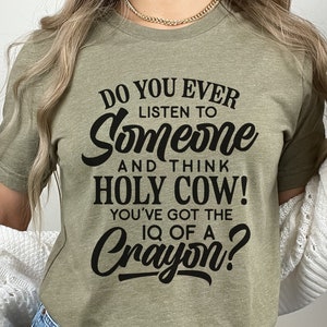 Może przedstawiać: Zielona koszulka z czarnym nadrukiem: "Do you ever listen to someone and think Holy Cow! You've got the IQ of a Crayon?"