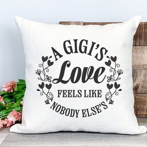 May include: A white cushion with black text that reads "A Gigi's Love Feels Like Nobody Else's" surrounded by a wreath of black hearts and floral designs.