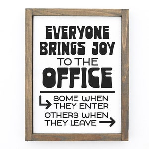 Puede incluir: Un cartel enmarcado con el texto "Everyone brings joy to the office. Some when they enter, others when they leave." El texto est&aacute; en un estilo de fuente retro.