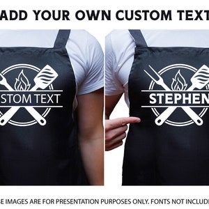 May include: Black apron with white text that says "CUSTOM TEXT" and a graphic of crossed grilling tools and a flame. The apron is being worn by a person.