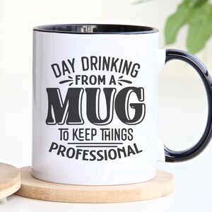 May include: White ceramic mug with a black handle and black rim. The mug has a black graphic that says "Day Drinking From A Mug To Keep Things Professional".