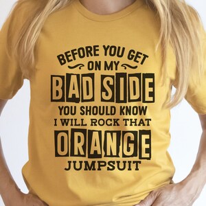 May include: A yellow t-shirt with the text "BEFORE YOU GET ON MY BAD SIDE YOU SHOULD KNOW I WILL ROCK THAT ORANGE JUMPSUIT" printed in black.