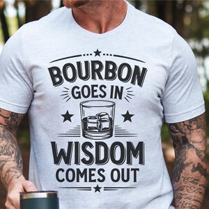 May include: A white t-shirt with a black graphic design that says "Bourbon goes in Wisdom comes out". The graphic also includes a glass of bourbon with ice cubes.