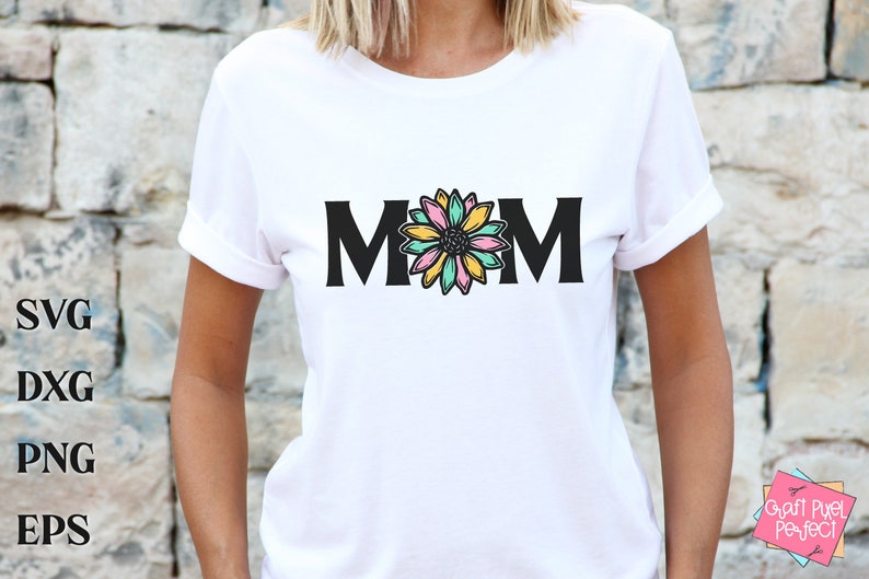 May include: White t-shirt with black text that reads "MOM" and a colorful flower graphic in the center.