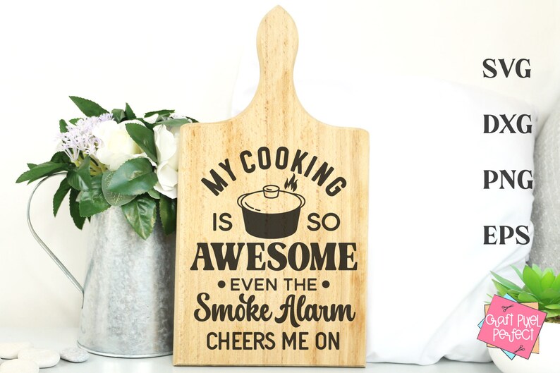 May include: A wooden cutting board with the text "My cooking is so awesome even the smoke alarm cheers me on".