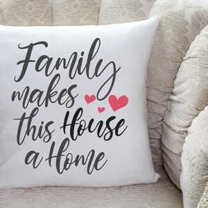May include: White throw pillow with black text that reads "Family makes this house a home" with pink hearts.