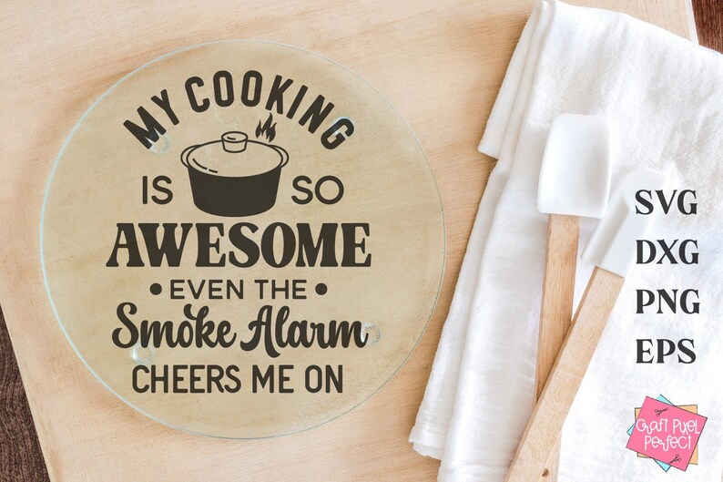 May include: A round glass cutting board with the text "My cooking is so awesome even the smoke alarm cheers me on". The text is in black and the cutting board is on a wooden surface.
