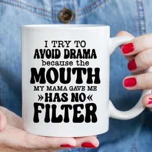 May include: White ceramic coffee mug with black text that reads "I try to avoid drama because the mouth my mama gave me >>has no<< filter".