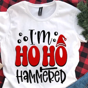 May include: White t-shirt with black text that reads "I'm Ho Ho Hammered" with a red Santa hat graphic.