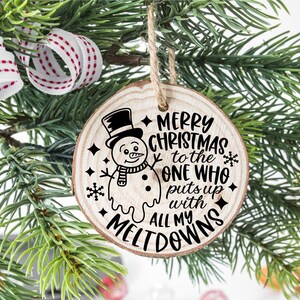 Puede incluir: Un adorno redondo de madera con un gr&aacute;fico de mu&ntilde;eco de nieve y el texto "Feliz Navidad al que aguanta todas mis rabietas".