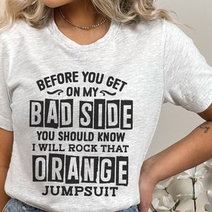 May include: A white t-shirt with black text that reads "Before you get on my bad side you should know I will rock that orange jumpsuit".
