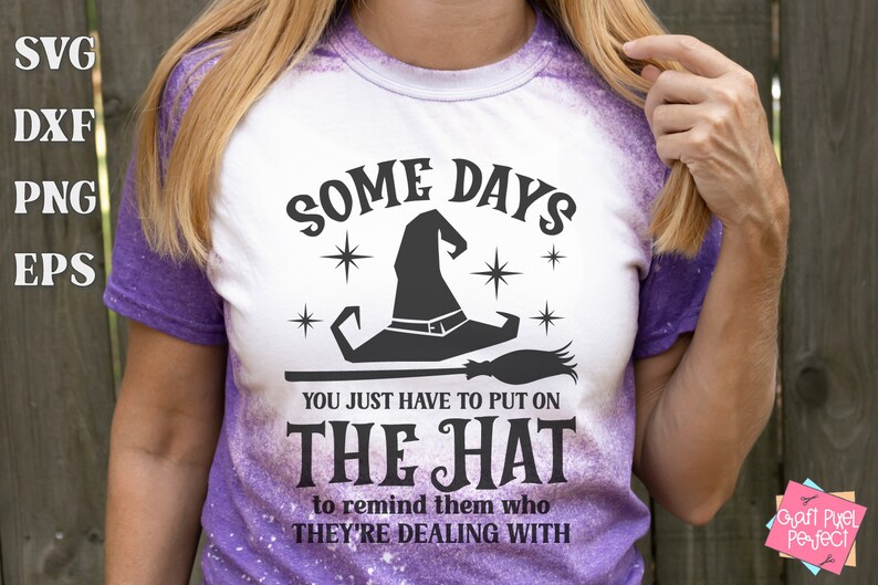 May include: A white t-shirt with a purple tie-dye design featuring a black witch hat and broom with the text "Some Days You Just Have To Put On The Hat To Remind Them Who They're Dealing With".