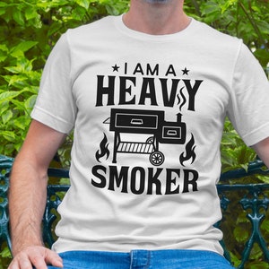 May include: White t-shirt with black text that reads "I am a Heavy Smoker" and a black silhouette of a smoker grill.