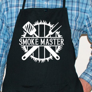 May include: A black apron with a white design of crossed grilling tools, a grill grate, flames, and the text "SMOKE MASTER".