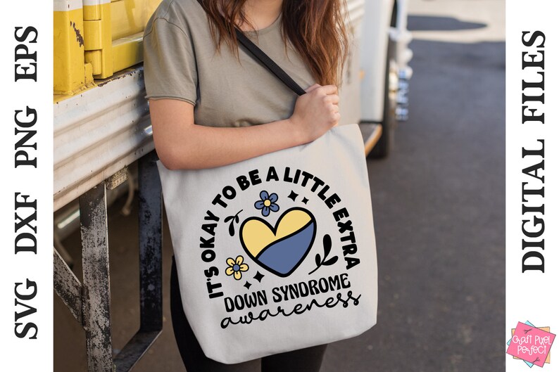 May include: A white tote bag with a black strap and a yellow and blue heart design. The text on the bag reads "It's okay to be a little extra Down Syndrome awareness".