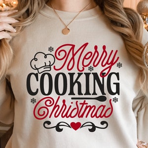 May include: A white sweatshirt with the text "Merry Cooking Christmas" in red and black lettering. A chef's hat is above the word "Cooking". A red heart is below the text.