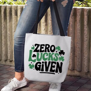 May include: A white tote bag with a green shamrock design and the text "Zero Lucks Given".