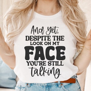 May include: A white t-shirt with black text that reads "And yet, despite the look on my face you're still talking".