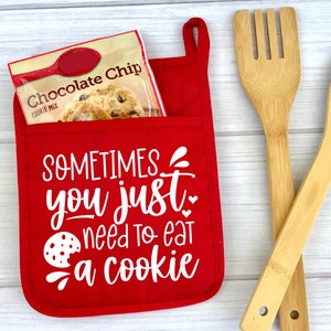 May include: Red oven mitt with a pocket that holds a bag of chocolate chip cookie mix. The oven mitt has the text "SOMETIMES you just need to eat a cookie" printed on it.
