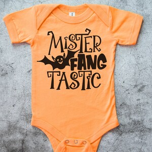 K&ouml;nnte beinhalten: Orangefarbener Baby-Strampler mit schwarzem Text "Mister Fang Tastic" und einer schwarzen Fledermausgrafik.