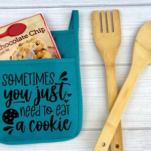 May include: Teal oven mitt with a pocket and the text "SOMETIMES you just need to eat a cookie" in black. A bag of chocolate chip cookie mix is in the pocket.