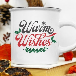 May include: White ceramic mug with a black rim and handle. The mug has a red and black design that says "Warm Wishes" with a snowflake and green holly leaves.