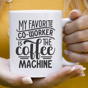 May include: White ceramic coffee mug with the text "MY FAVORITE CO-WORKER IS THE coffee MACHINE" in black. The mug is held by a person with a yellow background. The image also includes the text "SVG, DXF, EPS, PNG".
