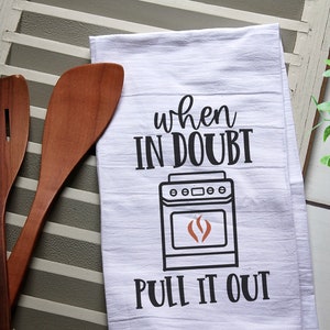 May include: White kitchen towel with black text that reads "When in doubt, pull it out."  A black and white illustration of a stove with a red flame is above the text.
