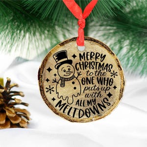 Puede incluir: Un adorno navide&ntilde;o redondo de madera con un mu&ntilde;eco de nieve derriti&eacute;ndose y el texto "Feliz Navidad al que aguanta todas mis rabietas".