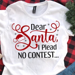 May include: White t-shirt with a red and black design that says "Dear Santa, I Plead No Contest..." with a Santa hat graphic.